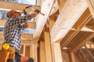 Carpenter hammering a nail to attach a board to a building at a construction site.