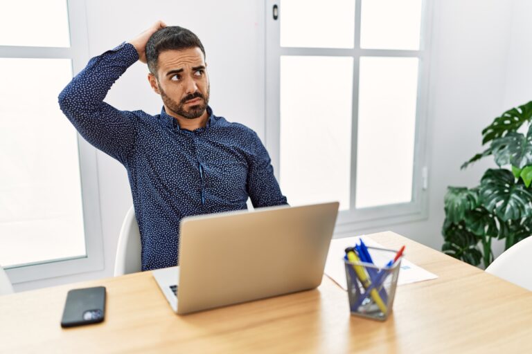 office man sitting at a desk and scratching his head with a confused look on his face